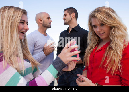 Deux sœurs partagent un moment tout en regardant quelque chose sur un téléphone cellulaire. Pendant ce temps, leurs pères gais partager leur propre moment. Banque D'Images