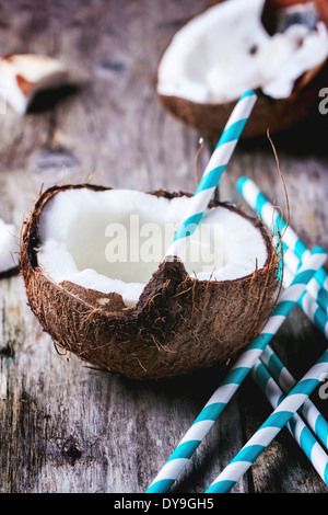 Broken coconut avec du lait de coco et les pailles cocktail sur la vieille table en bois Banque D'Images