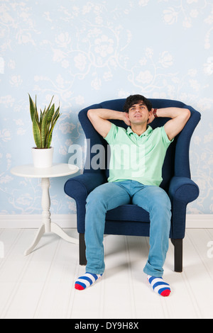 Jeune homme assis dans un fauteuil bleu en vivant à domicile Banque D'Images