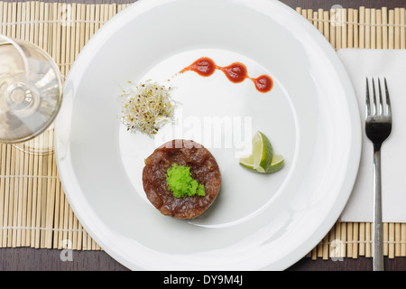 Saumon avec sauce tartare et de la chaux sur plaque simple blanche et un verre de vin blanc. Banque D'Images