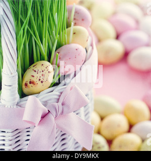 Petit aperçu des oeufs de Pâques dans un panier blanc vert avec l'herbe fraîche sur fond rose de couleur pastel avec vintage édition texturé Banque D'Images