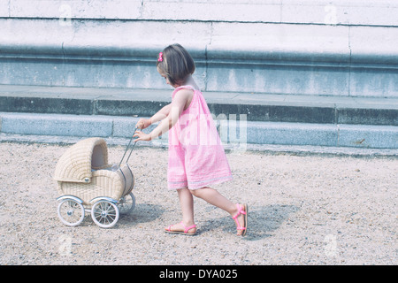 Petite fille poussant poussette miniature Banque D'Images