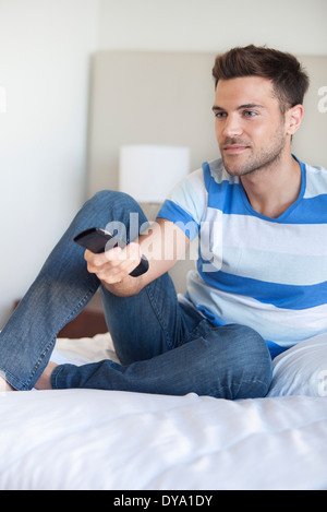 Young man reclining on bed watching tv Banque D'Images