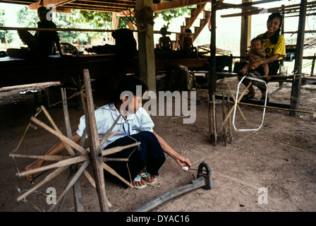 Laos jeune fille accroupie roue tournante de canette femme bebe look sur l'ombre terre soleil lumière marbre roue en bois Banque D'Images