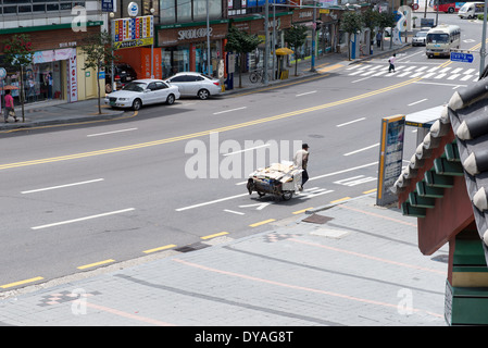 Street view à Yeosu, Corée du Sud, avec des voitures et un homme tirant un chariot avec du papier Banque D'Images