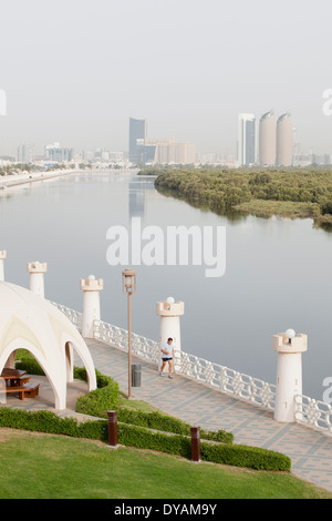 Un homme s'exécute sur une passerelle dans un parc le long de la rue Al Salam, et les mangroves avec la ville d'Abu Dhabi dans l'arrière-plan. Banque D'Images