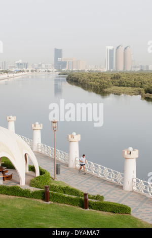 Un homme s'exécute sur une passerelle dans un parc le long de la rue Al Salam, et les mangroves avec la ville d'Abu Dhabi dans l'arrière-plan. Banque D'Images