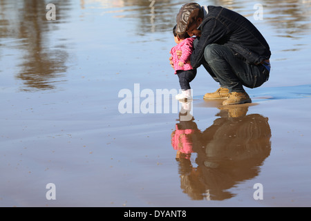 Plus coying Père fille enfant sur une plage de sable humide à Essaouira, Maroc, de ne pas voir une vague venant jusqu'à ce tout dernier minu Banque D'Images