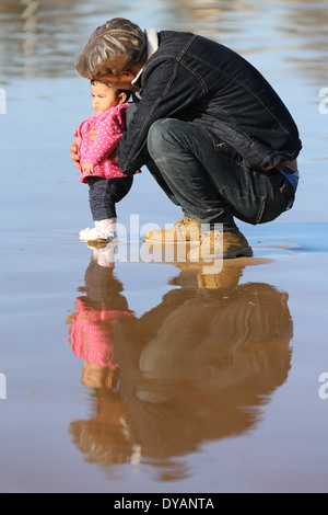 Plus coying Père fille enfant sur une plage de sable humide à Essaouira, Maroc, de ne pas voir une vague venant jusqu'à ce tout dernier minu Banque D'Images