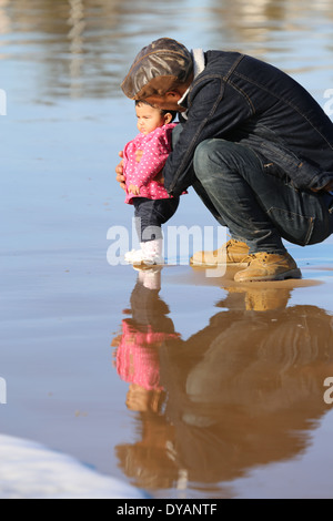 Plus coying Père fille enfant sur une plage de sable humide à Essaouira, Maroc, de ne pas voir une vague venant jusqu'à ce tout dernier minu Banque D'Images