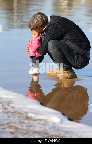 Plus coying Père fille enfant sur une plage de sable humide à Essaouira, Maroc, de ne pas voir une vague venant jusqu'à ce tout dernier minu Banque D'Images