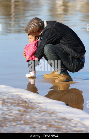 Plus coying Père fille enfant sur une plage de sable humide à Essaouira, Maroc, de ne pas voir une vague venant jusqu'à ce tout dernier minu Banque D'Images