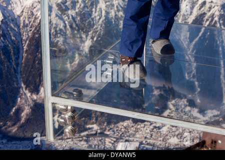 Un touriste se trouve dans le 'Step dans le Vide' boîte de verre sur l'Aiguille du Midi (3842 m) sommet de montagne au-dessus de Chamonix Mont-Blanc Banque D'Images