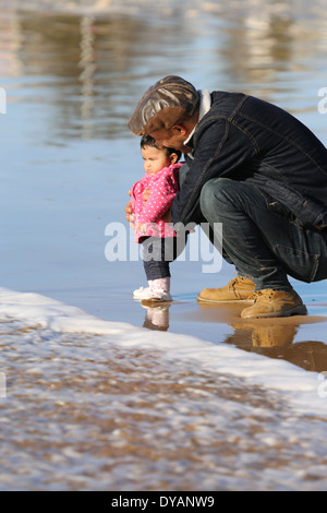 Plus coying Père fille enfant sur une plage de sable humide à Essaouira, Maroc, de ne pas voir une vague venant jusqu'à ce tout dernier minu Banque D'Images