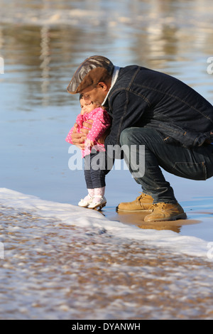 Plus coying Père fille enfant sur une plage de sable humide à Essaouira, Maroc, de ne pas voir une vague venant jusqu'à ce tout dernier minu Banque D'Images