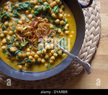 Curry de pois chiches et les épinards avec oignons caramélisés dans une marmite en fonte sur une table en chêne Banque D'Images