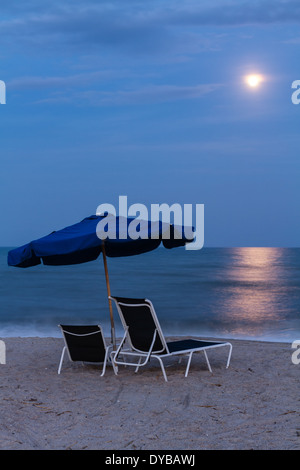 Pleine lune s'élève au-dessus de comme ensemble de chaises de plage et parasol sur la plage sur Amelia Island, en Floride. Banque D'Images