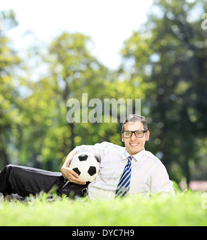 Jeune homme allongé sur l'herbe et holding a football in park Banque D'Images