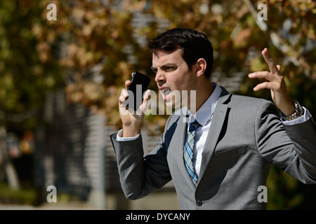 Un jeune homme d'affaires en tailleur criant avec colère à quelqu'un,les bras tout en maintenant son téléphone cellulaire.Un concept portrait en colère Banque D'Images