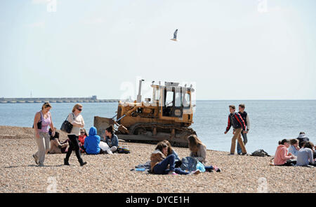 Ouvriers l'exploitation d'un mechanical digger aux côtés de visiteurs profiter du beau temps de printemps chaud sur la plage de Brighton Banque D'Images