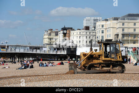 Ouvriers l'exploitation d'un mechanical digger aux côtés de visiteurs profiter du beau temps de printemps chaud sur la plage de Brighton Banque D'Images