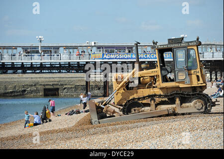 Ouvriers l'exploitation d'un mechanical digger aux côtés de visiteurs profiter du beau temps de printemps chaud sur la plage de Brighton Banque D'Images