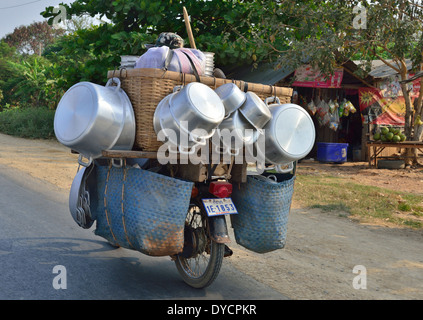 Homme cambodgien sur une petite moto surchargée (selon les normes européennes) avec des marchandises de marché de casseroles et de poêles, Battambang, Cambodge Banque D'Images