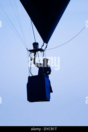 Un homme à l'essai d'un ballon à air chaud d'une personne passant en silhouette devant un ciel bleu voilé Banque D'Images