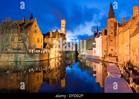 Canaux de Bruges Vieille Ville Bruges Belgique | BRUGES, Belgique — Le beffroi s'élève au-dessus du canal Reien à l'heure bleue, son lanterne octogonale inondée de lumière ancrant une vue largement considérée comme le cliché classique de la ville. Construit par étapes après un incendie en 1280, la tour mesure 272 pieds (83 m) de haut et penche d'environ 34 pouces (87 cm) vers Wollestraat. Banque D'Images