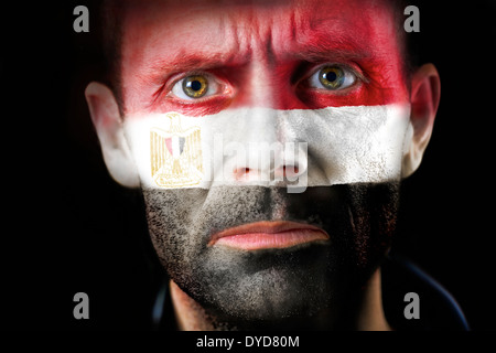 Un regard intense d'un homme avec le visage peint avec le drapeau égyptien. Banque D'Images