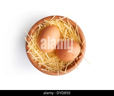 Deux oeufs de poules frais sur un peu de paille dans un bol en bois sur un fond blanc. Banque D'Images