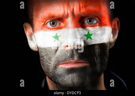 Un regard intense d'un homme avec le visage peint avec le drapeau syrien. Banque D'Images