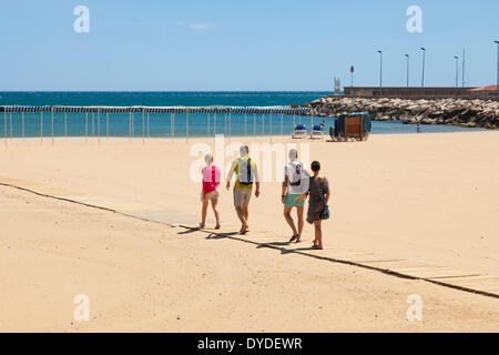 Quatre personnes marchant sur lattes de bois rampe d'accès de la plage à Cambrils en Espagne. Banque D'Images