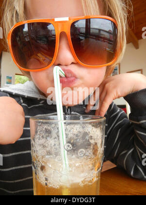 Une happy boy blowing bubbles dans le jus de pomme. Banque D'Images