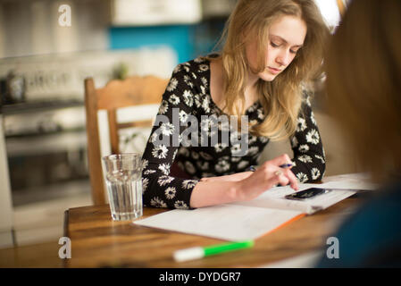 Une jeune fille de 16 ans faire des mathématiques devoirs sur la table de la cuisine. Banque D'Images