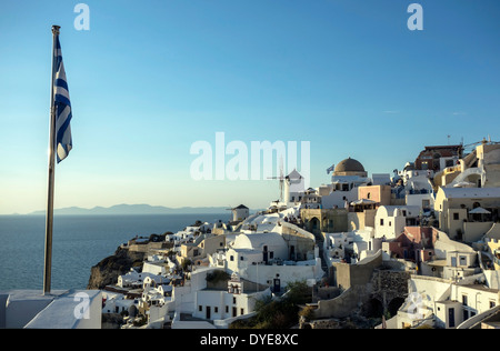Vue panoramique du village d'Oia à Santorin, Grèce, avec le drapeau grec agitant Banque D'Images