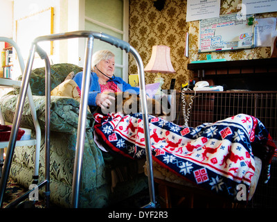 Ancien femme assise dans sa chaise avec son chat sur ses genoux et audio téléphones mobiles dans ses oreilles Banque D'Images