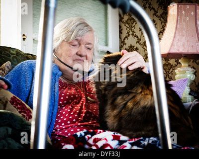 Ancien femme assise dans sa chaise avec son chat sur ses genoux et audio téléphones mobiles dans ses oreilles Banque D'Images