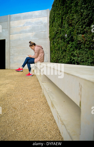 Jeune femme était assise à l'extérieur des SMS sur téléphone mobile Banque D'Images