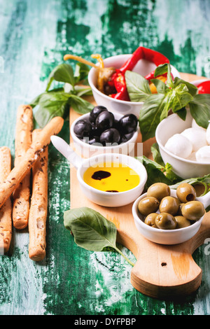 Olives antipasti mixtes et mozzarella servi sur planche à découper en bois sur table en bois vert. Banque D'Images