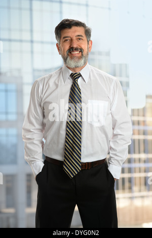 Portrait of senior businessman with hands in pockets en face de grande fenêtre in office Banque D'Images