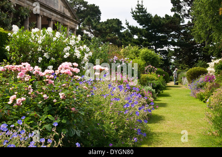 Un jardinier admire son travail à la frontière large bordée de plantes herbacées dans les jardins de Kiftsgate court dans les Cotswolds, Gloucestershire, Angleterre Banque D'Images