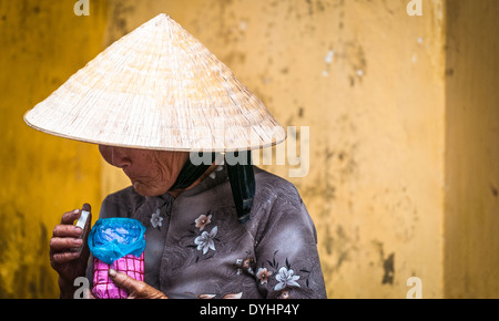 Pauvre vieille femme portant chapeau conique et robe traditionnelle asiatique. Dame vietnamienne holding pot rose et bleu. Banque D'Images