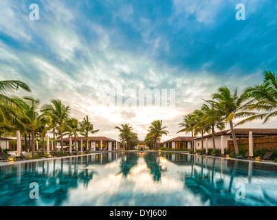 Maisons et piscine au milieu du resort au Vietnam, en Asie. Reflet de palmiers verts et ciel bleu avec des nuages dans l'eau. Banque D'Images