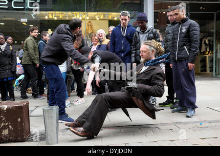 Manchester, UK. 19 avril 2014. Un jeune homme tente d'expliquer à ses amis la façon dont un artiste de rue défiant la gravité est en mesure de montrer son talent en face de passant en rue du marché. Artiste de rue Manchester, UK 19 avril 2014 Crédit : John Fryer/Alamy Live News Banque D'Images