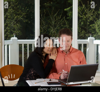 Photo de près d'âge mûr qui travaille à la maison avec un ordinateur portable, une calculatrice et documents sur le dessus de table et de grandes fenêtres en arrière-plan Banque D'Images