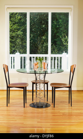 Photo verticale de la petite salle à manger avec parquet en chêne rouge, table en verre, chaises en bois, de grandes fenêtres et des plantes de bambou Banque D'Images