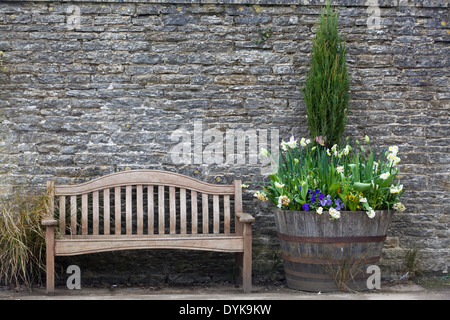 Banc en bois contre un mur de pierre avec un baril pot de fleurs Banque D'Images