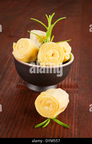 L'artichaut en noir bol avec du romarin frais sur fond de bois sombre. Manger culinaire. Banque D'Images