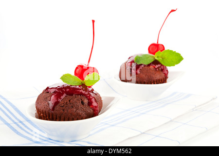 Deux délicieux muffins au chocolat maison décorée avec de la confiture, de cerise et de feuilles de menthe fraîche sur un chiffon de cuisine. Banque D'Images